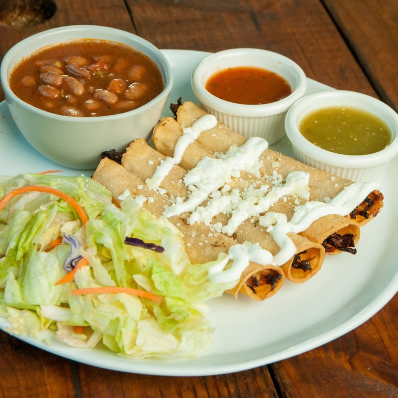 Taquitos with sour cream and cheese, served with a side salad, beans, and two dipping sauces.